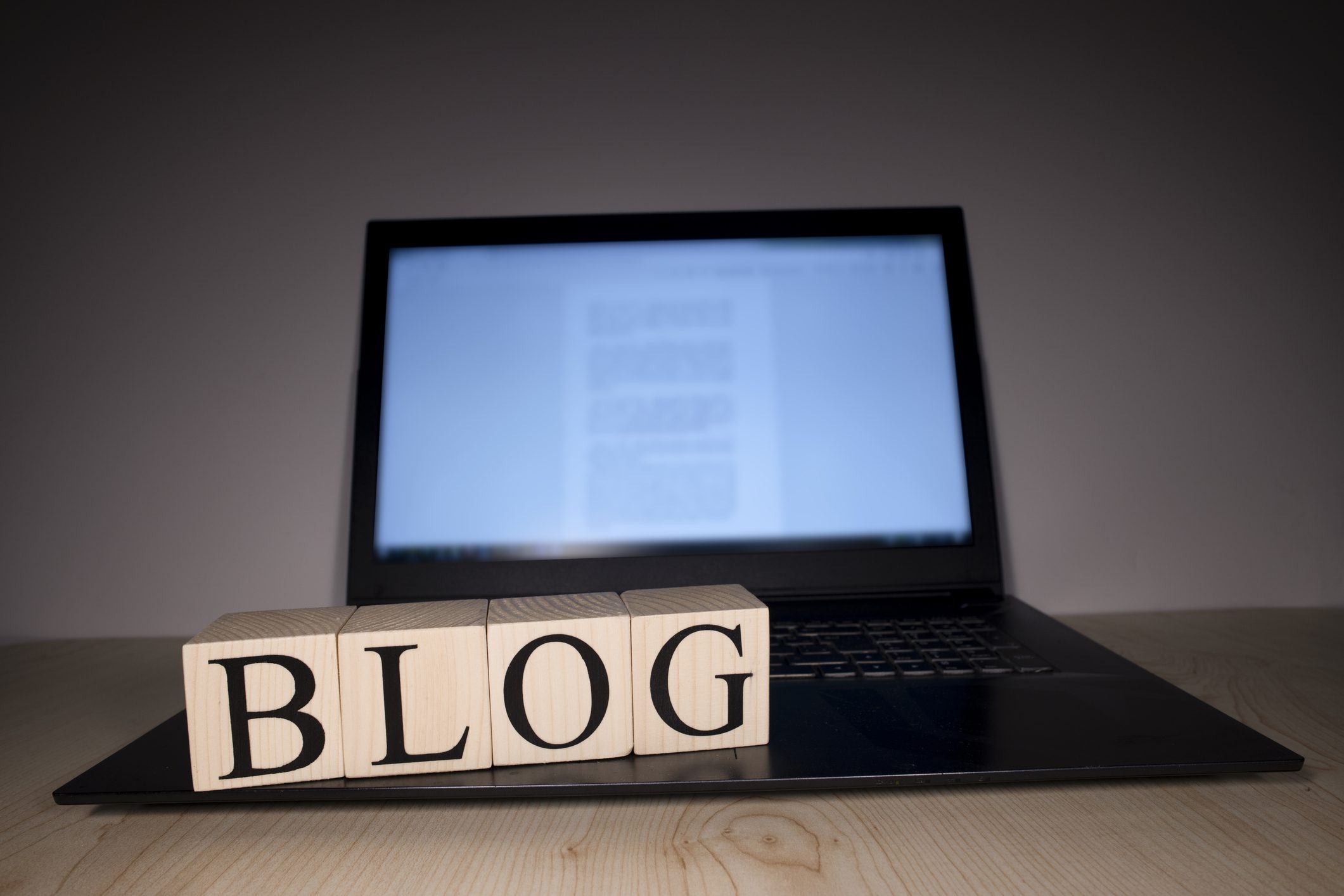 The laptop screen on the table is open. Blog word on wooden cubes on laptop. Photographs were taken in the spotlight.