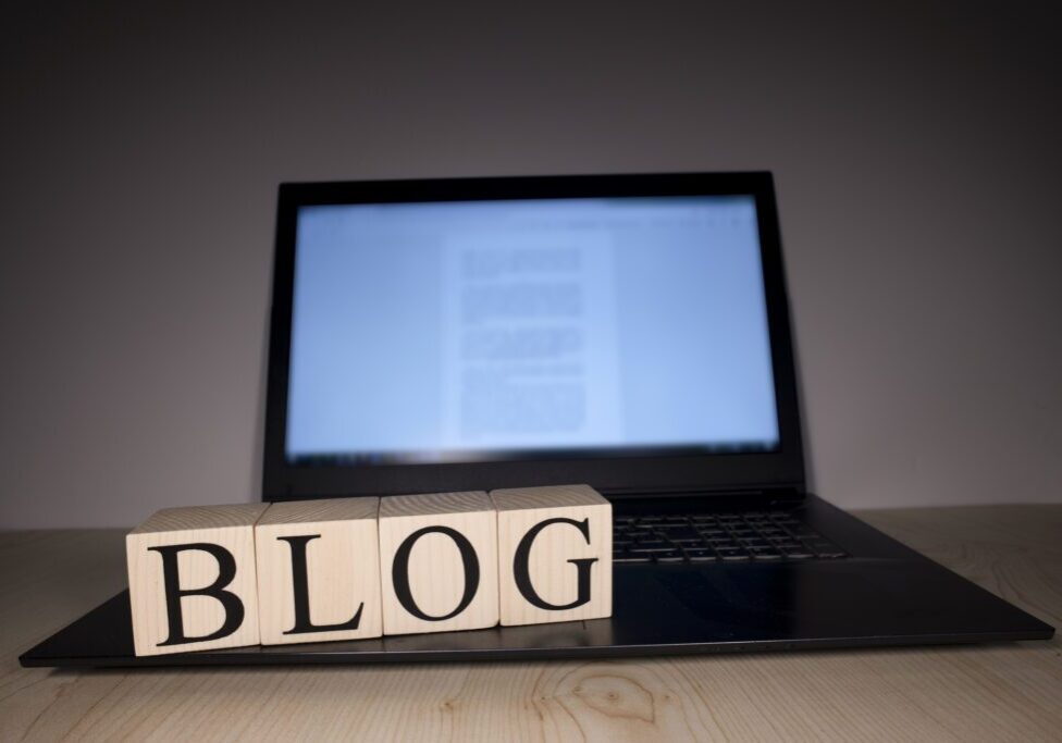 The laptop screen on the table is open. Blog word on wooden cubes on laptop. Photographs were taken in the spotlight.